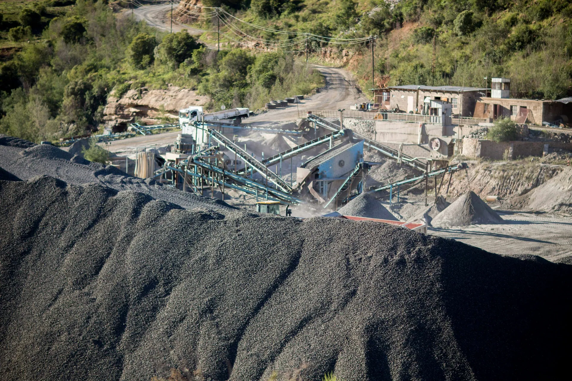Rock crushing and screening plant with dark aggregate stockpiles on a hillside