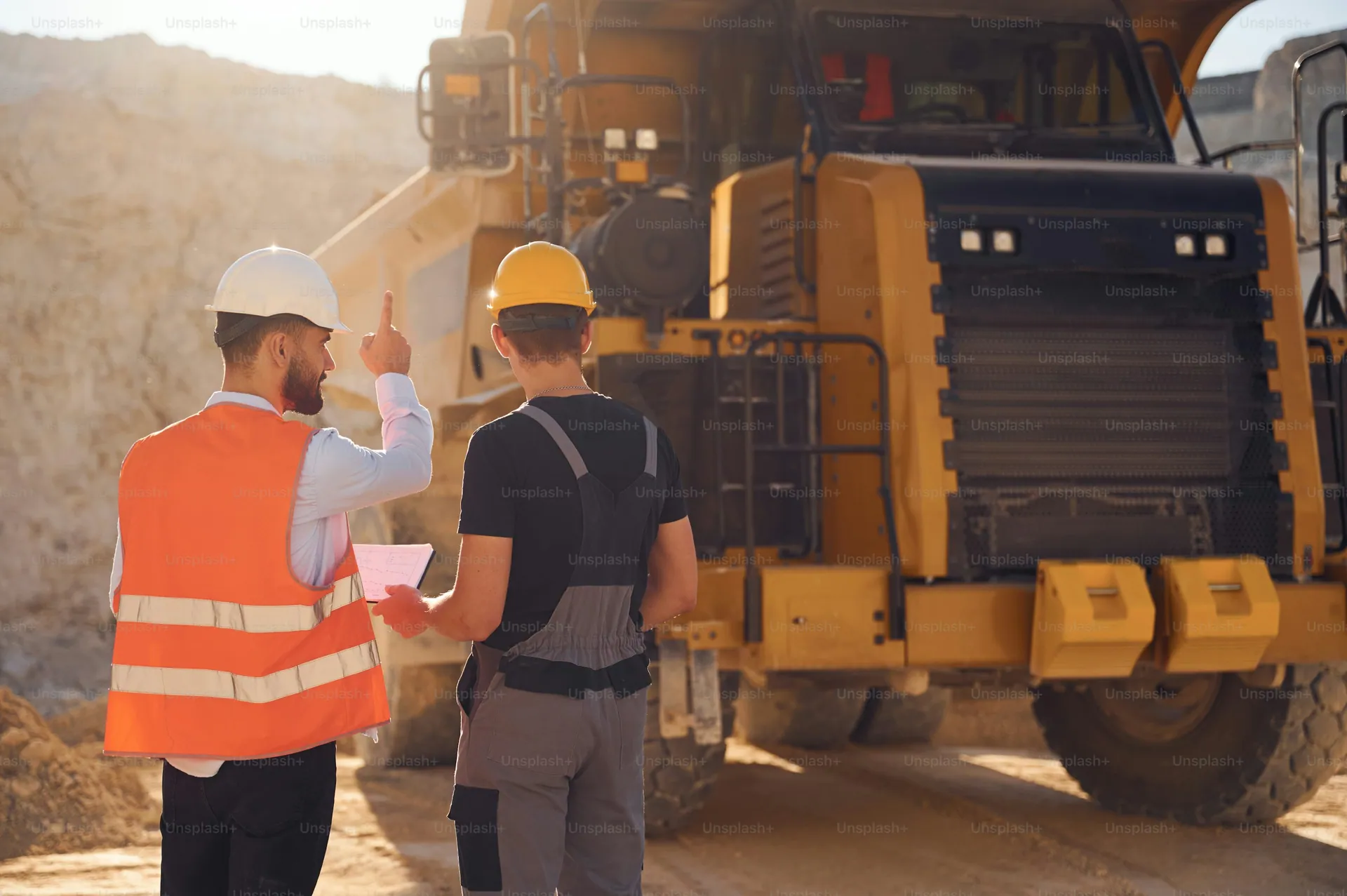 Two workers reviewing documents in front of a large haul truck at a mine site